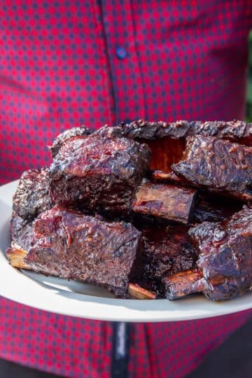 Juicy beef short rib with crispy bark and glaze on a wooden board.