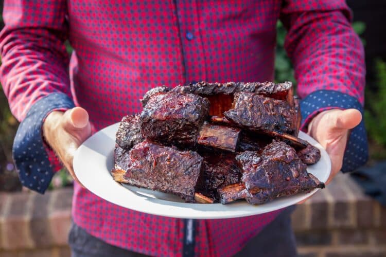 Juicy beef short rib with crispy bark and glaze on a wooden board.
