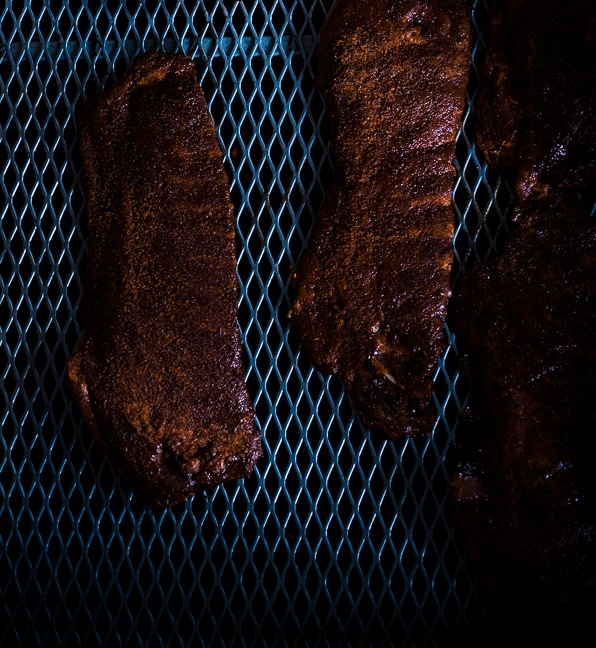 Smoked spareribs with a caramelized glaze, sliced and arranged on a wooden board.