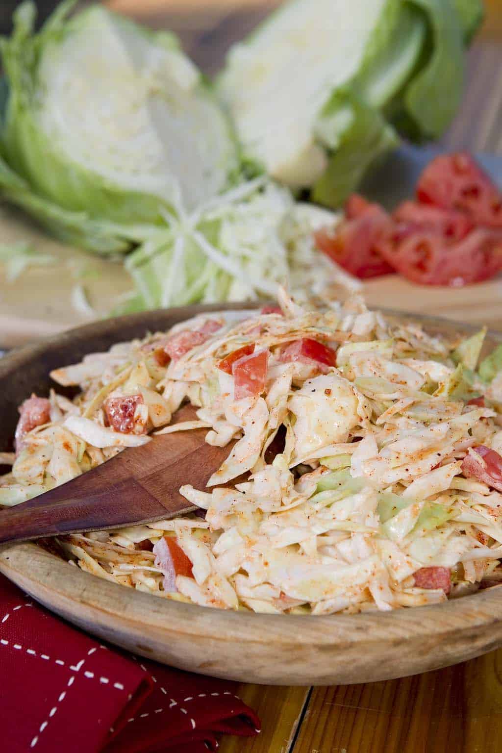Bowl of creamy cole slaw with visible cabbage, onion, and tomato.