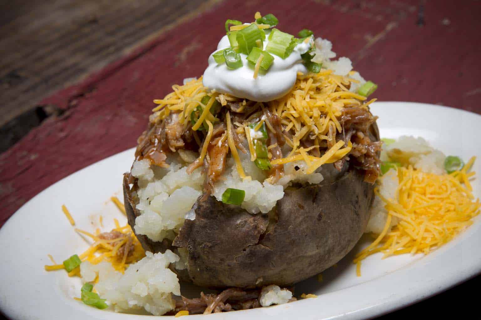 Barbecue-stuffed baked potatoes topped with cheddar and scallions on a wooden board.
