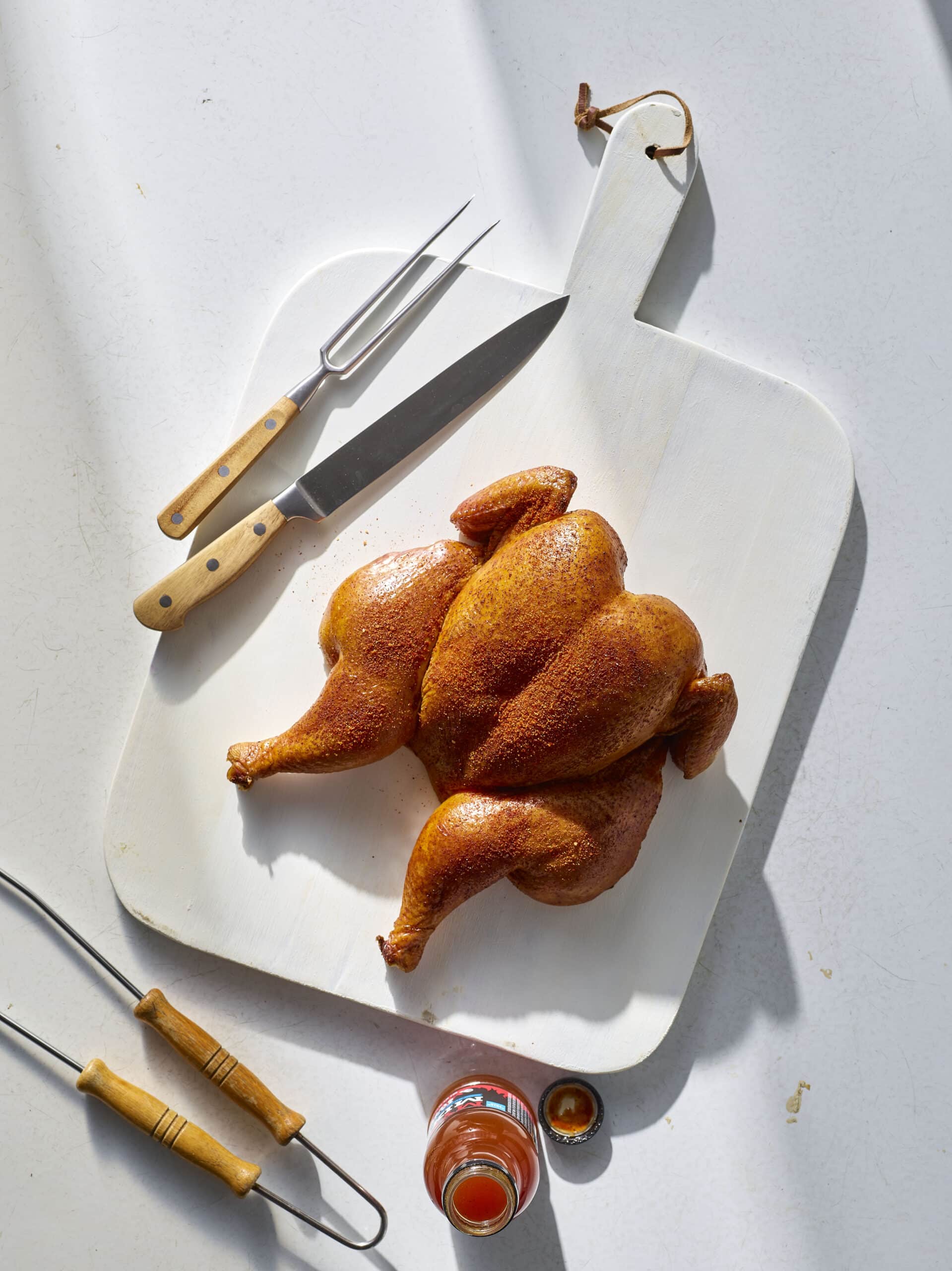 Smoked whole chicken with crispy skin and BBQ rub, carved on a wooden board