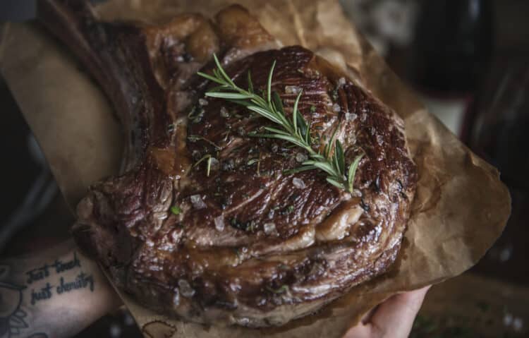 Grilled marinated ribeye steak with grill marks on a cutting board.