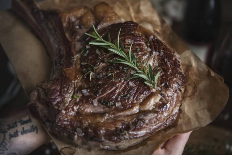 Grilled marinated ribeye steak with grill marks on a cutting board.