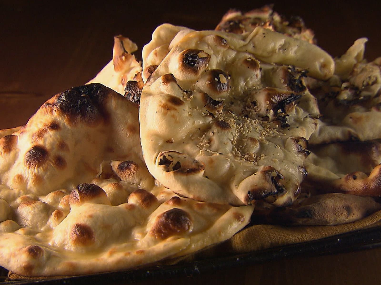 Layered naan flatbreads grilled and brushed with butter, stacked on a serving board.