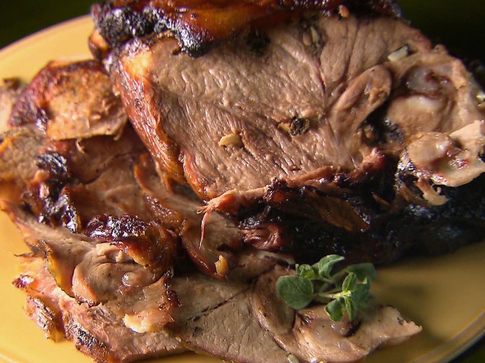 A beautifully plated dish featuring Keyan-style split-roasted lamb. The lamb is golden-brown with a charred, crispy exterior, served alongside fresh herbs and colorful accompaniments on a rustic wooden table.