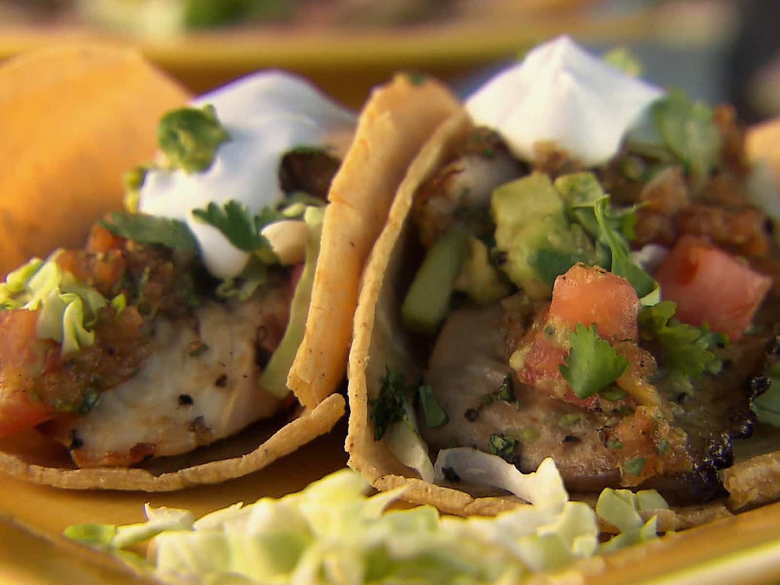 Grilled fish tacos topped with cabbage, salsa, avocado, and lime in corn tortillas.