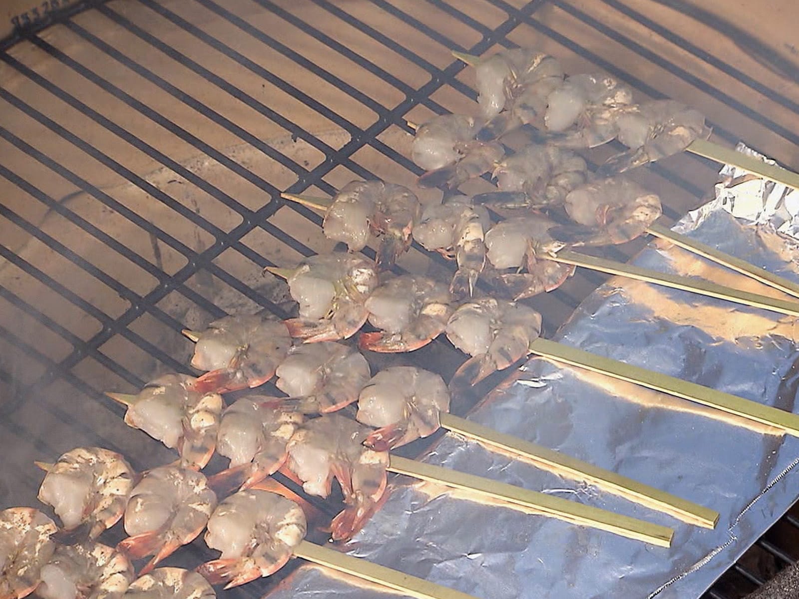 Grilled shrimp wrapped in prosciutto and basil on a platter with lemon wedges