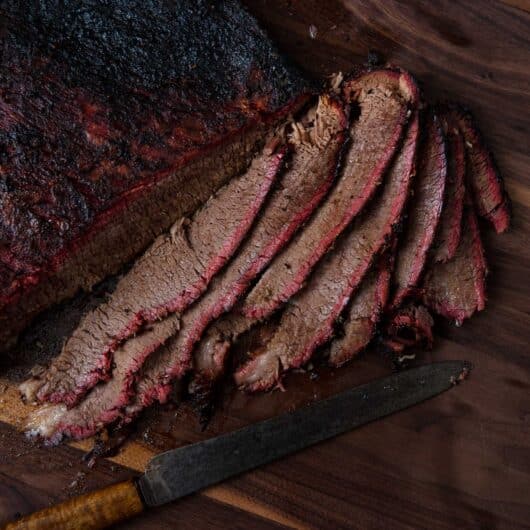 Myron Mixon’s smoked brisket sliced on a cutting board with visible smoke ring and bark
