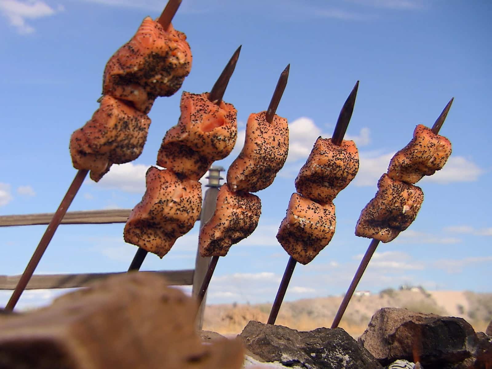 Salmon fillets skewered and grilled upright over an open flame.