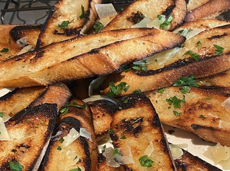 Slices of fire-grilled garlic bread with golden char and melted garlic butter.