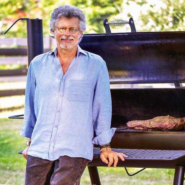 Steven Raichlen standing in front of an open smoker with a brisket inside, looking toward the camera