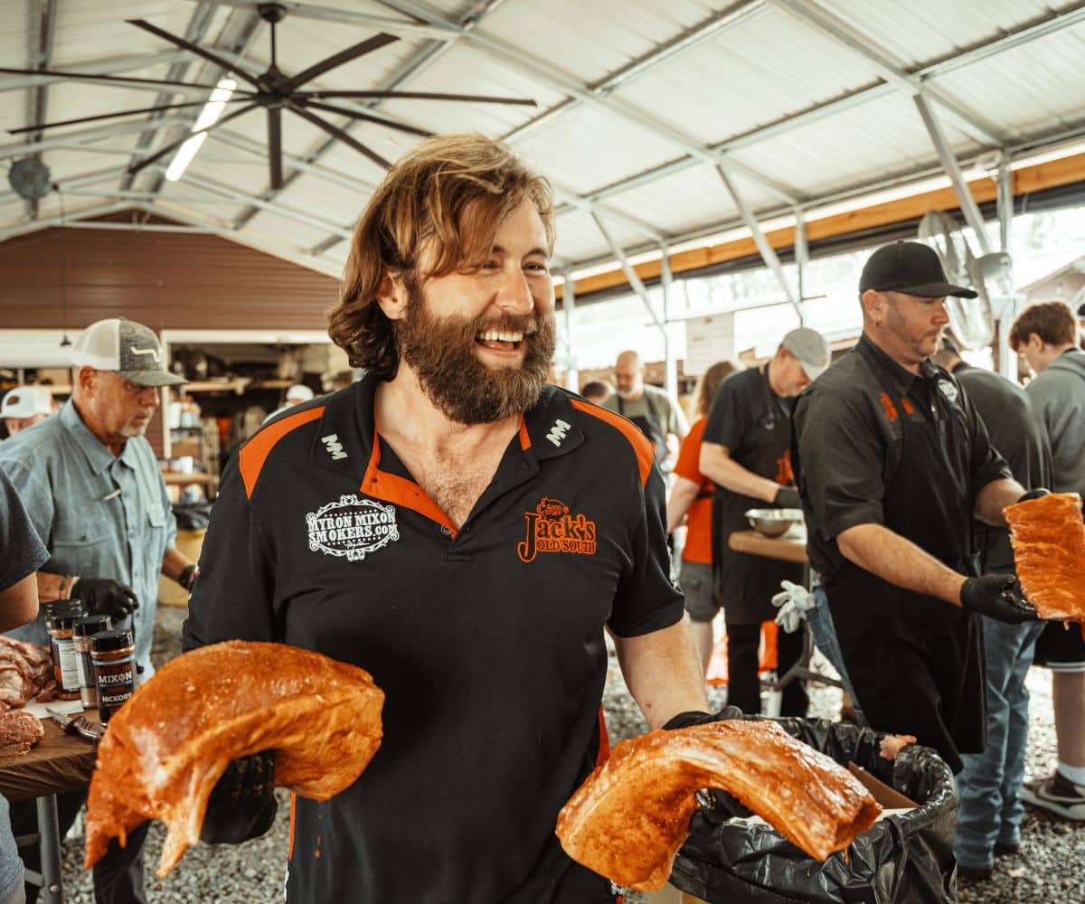 Steven Raichlen standing in front of an open smoker with a brisket inside, looking toward the camera