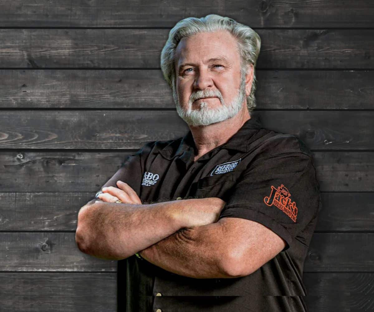 Portrait of Myron Mixon leaning on a car, arms crossed, staring confidently at the camera